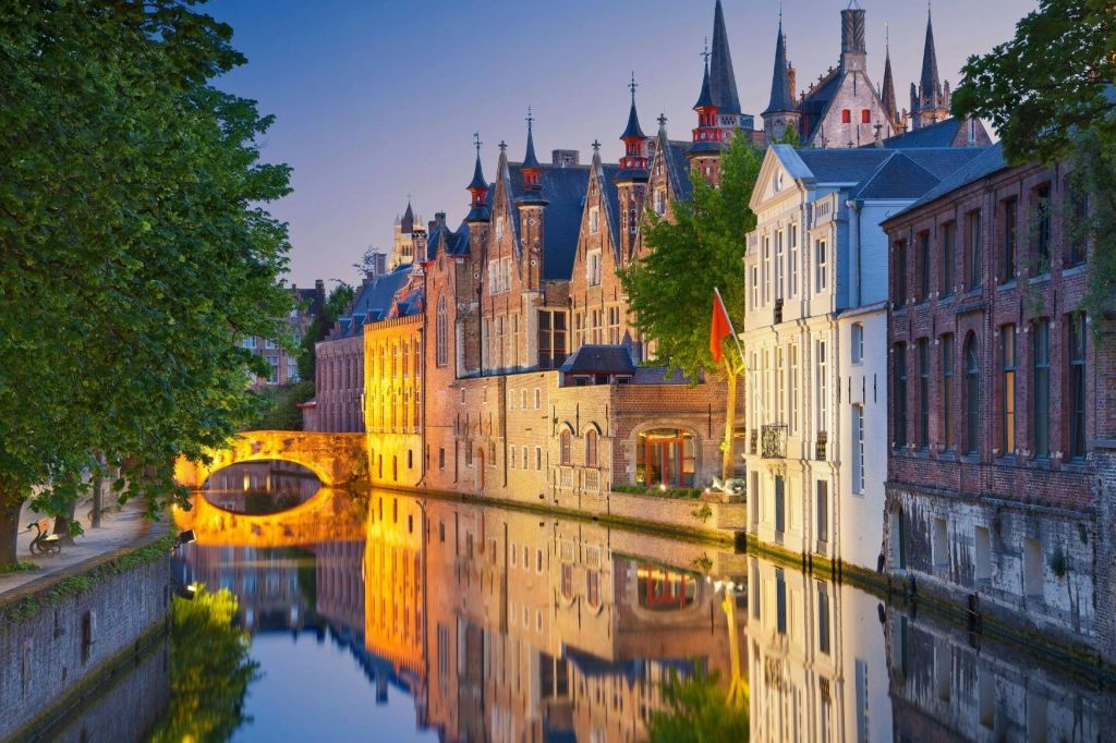 해질 무렵 고요한 운하에 반사된 역사적인 건물로 화려한 건축물과 석조 다리를 배경으로 합니다.