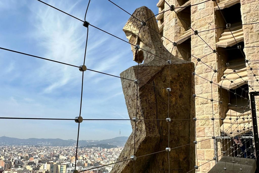 푸른 하늘 아래 건물과 언덕이 있는 도시 경관을 배경으로 그물에 걸린 커다란 석상.