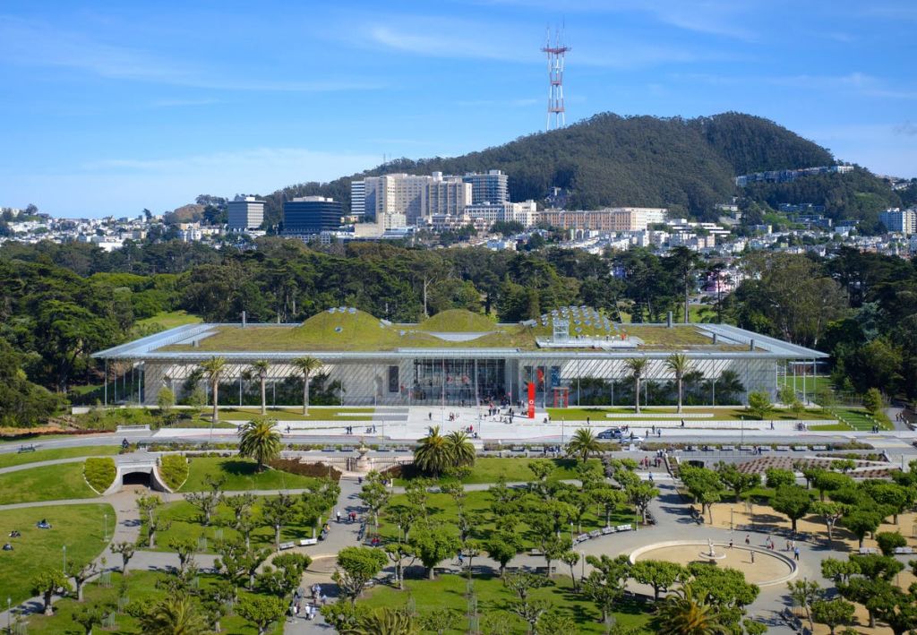녹색 지붕이 있는 큰 건물은 많은 사람들이 있는 공원으로 둘러싸여 있습니다. 언덕, 높은 건물, 탑이 배경입니다.