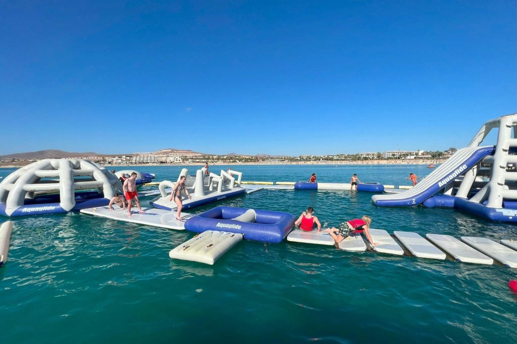 화창한 날 넓은 물속에서 미끄럼틀과 장애물이 있는 커다란 팽창식 워터파크를 즐기는 사람들.