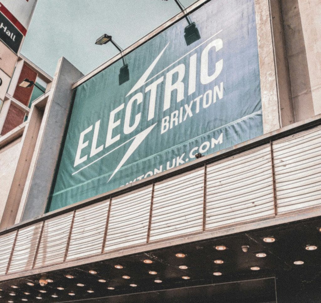 가로등 아래 건물 외관에 웹사이트 URL이 있는 "Electric Brixton" 이라는 대형 야외 표지판.
