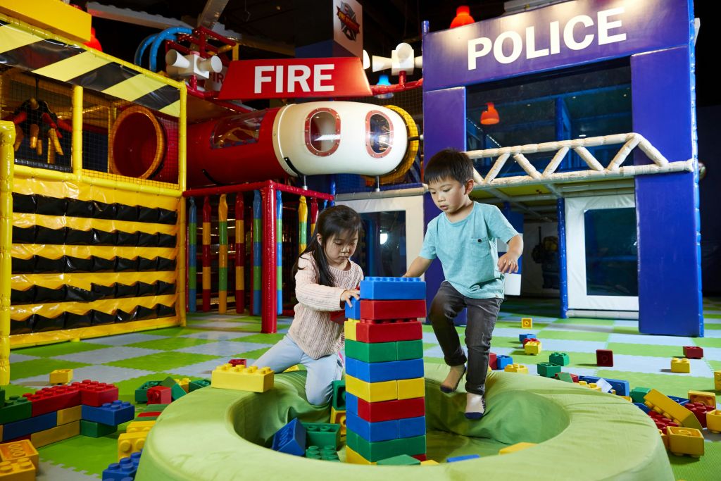 화재와 경찰을 주제로 한 구조물이 있는 실내 놀이터에서 두 어린이가 크고 화려한 빌딩 블록을 가지고 놀고 있습니다.