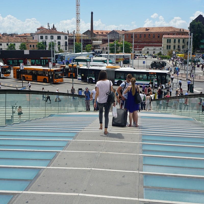 버스와 건물을 배경으로 분주한 거리를 향해 유리와 콘크리트 계단을 내려가는 사람들.