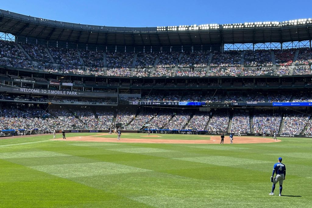 화창한 하늘 아래 필드에 군중과 선수들이 보이는 대형 경기장에서 진행 중인 야구 경기.