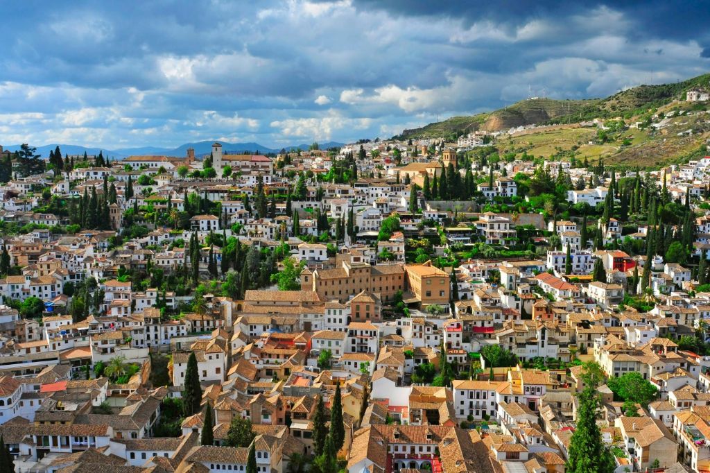 빽빽한 흰색 건물, 갈색 타일 지붕, 흐린 하늘 아래 푸른 나무가 있는 오래된 마을의 공중 전망.