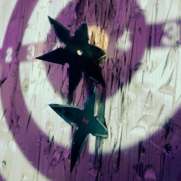 자주색과 흰색 불빛이 비추는 목재 타겟 보드에 검은색 던지는 별 두 개가 박혀 있습니다.