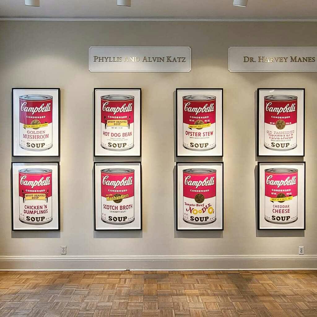 6개의 액자에 담긴 캠벨의 수프 캔 프린트가 갤러리 벽에 걸려 있으며 위의 이름은 "필리스와 앨빈 카츠" 와 "하비 갈기 박사" 입니다.
