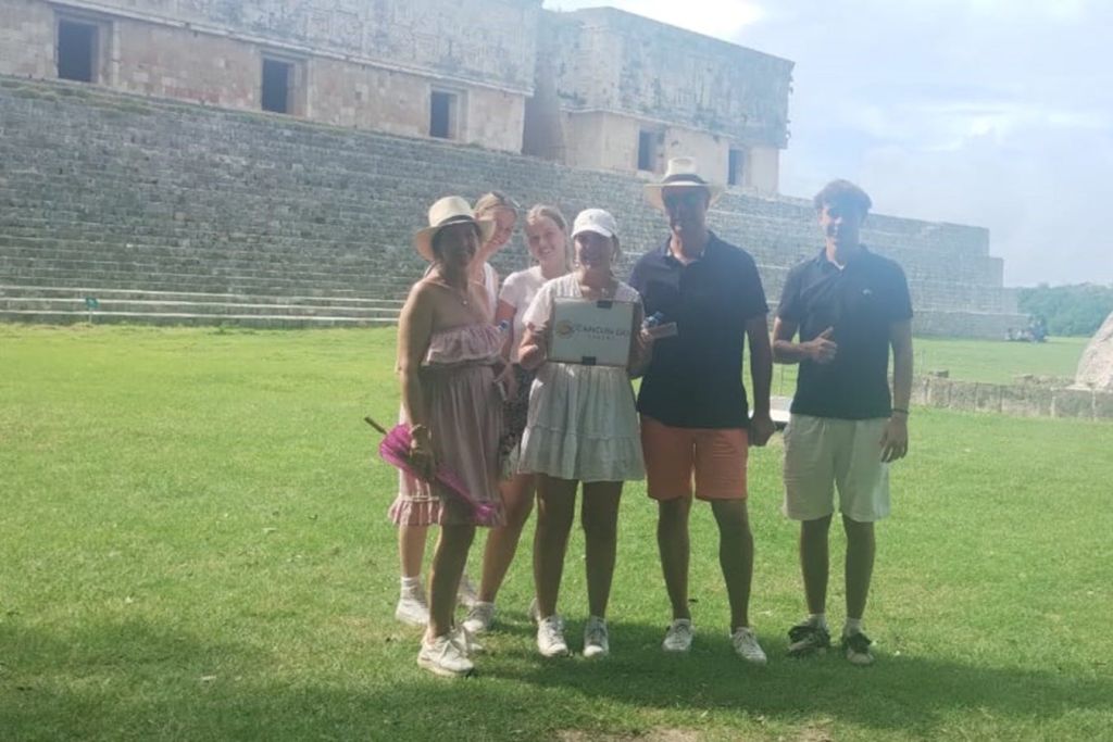 정교한 조각과 계단이 있는 고대 석조 건물 앞 잔디밭에는 5명의 사람들이 서 있습니다.