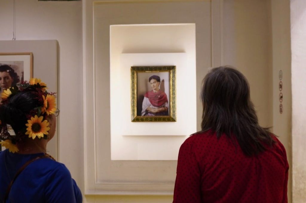 두 사람은 조명이 밝은 디스플레이 벽에 걸린 전통 복장을 한 여성의 액자 초상화를 관찰합니다.