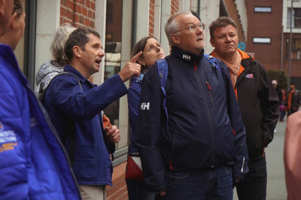 야외 복장을 한 몇몇 사람들이 도시 거리에 서서 관심을 가지고 위를 바라보고 있습니다.