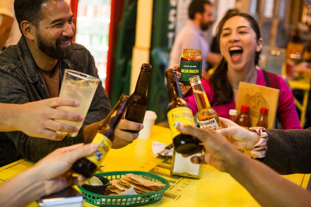 한 무리의 사람들이 노란색 테이블에서 맥주병을 흔들며 캐주얼한 분위기에서 활기찬 식사를 즐기고 있습니다.