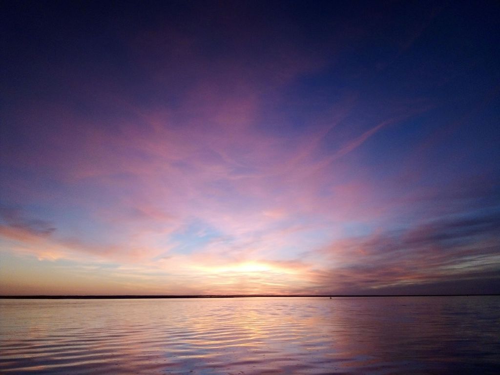 하늘이 분홍색, 주황색, 보라색으로 가득한 잔잔한 물 위의 고요한 석양.