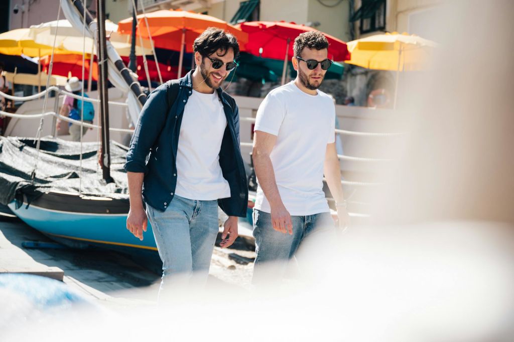선글라스와 캐주얼한 옷을 입은 두 남성이 밝은 색상의 우산을 배경으로 야외에서 걷고 있습니다.