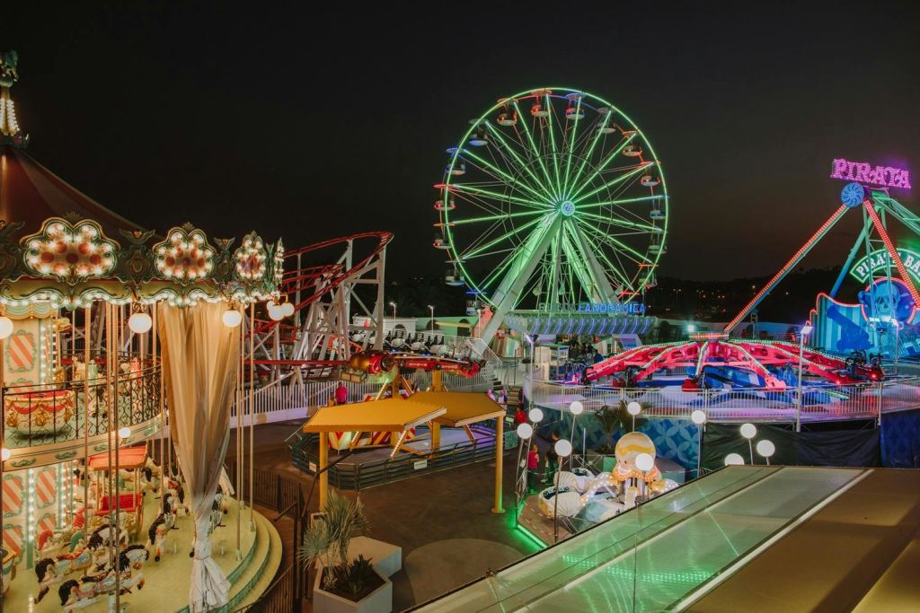 야간에는 불이 켜진 관람차, 회전목마, 롤러코스터, 화려한 조명이 있는 놀이공원이 있습니다.