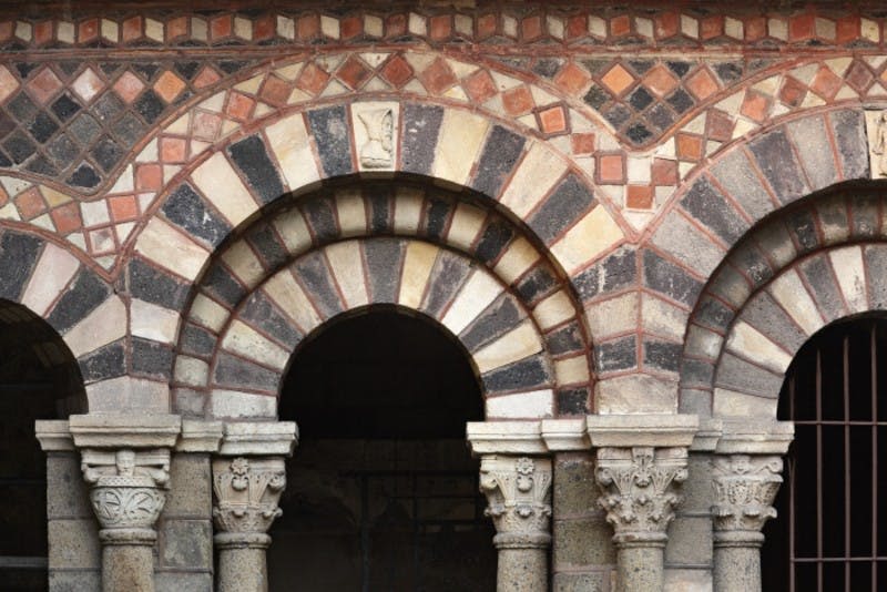 검은색과 흰색의 돌, 장식 기둥, 그리고 위의 상세한 모자이크 패턴이 교대로 표시된 아치형 돌 출입구.