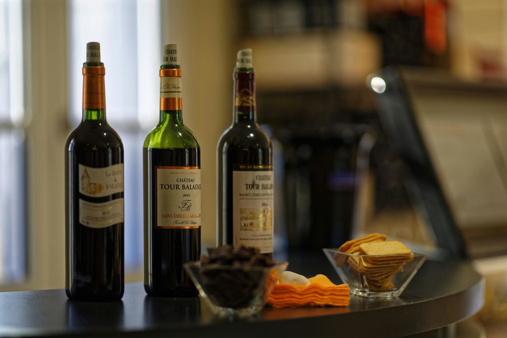 조명이 어두운 검은색 표면에 와인 3병, 간식 2그릇, 접힌 냅킨이 놓여 있습니다.