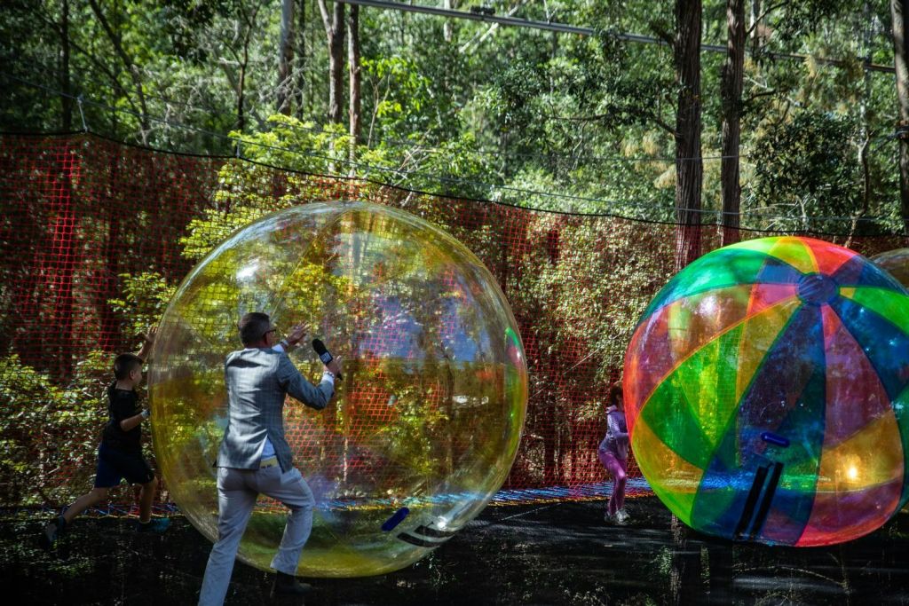 나무와 메쉬 울타리를 배경으로 야외에 있는 크고 투명한 팽창식 볼 안에 두 사람이 있습니다.