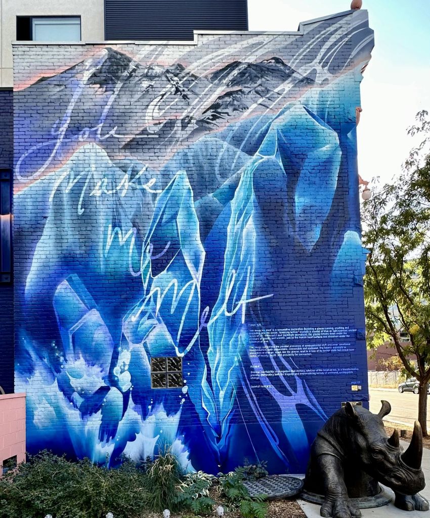 푸른 얼음층과 산이 특징인 벽돌 벽의 활기찬 벽화로, 텍스트가 디자인에 통합되어 있습니다.