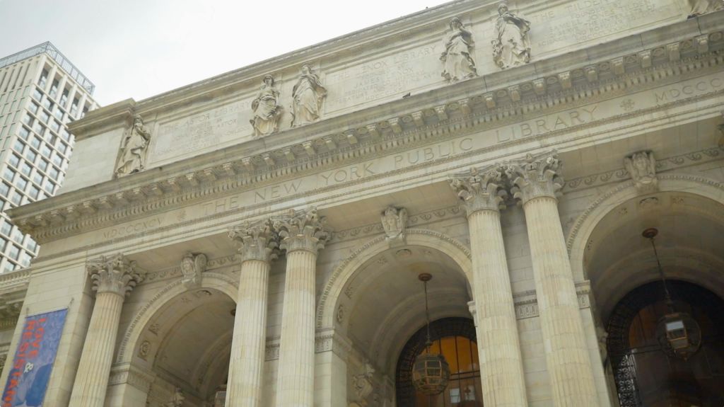 흐린 하늘 아래 기둥, 동상, 건축학적 디테일이 돋보이는 뉴욕 공립 도서관의 정면.