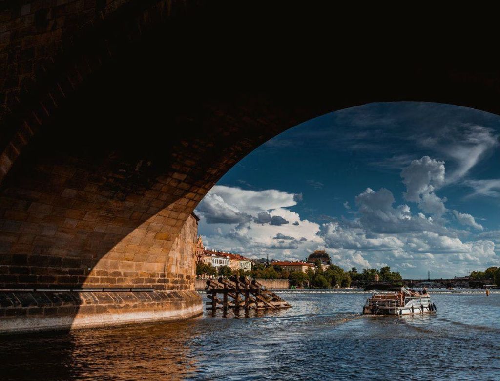 역사적인 건물이 있는 강가의 커다란 돌다리 아래를 지나가는 보트와 구름을 배경으로 한 푸른 하늘.