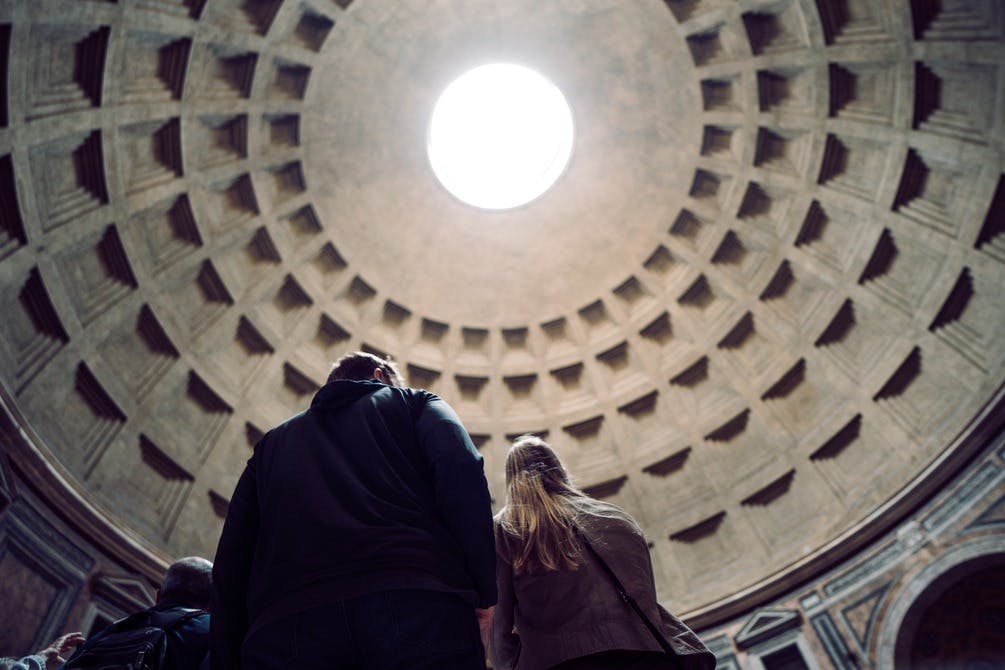 두 사람이 커다란 원형의 돔형 천장을 올려다보고 있으며, 웅장한 건축물 내부에는 중앙의 오큘러스가 있습니다.