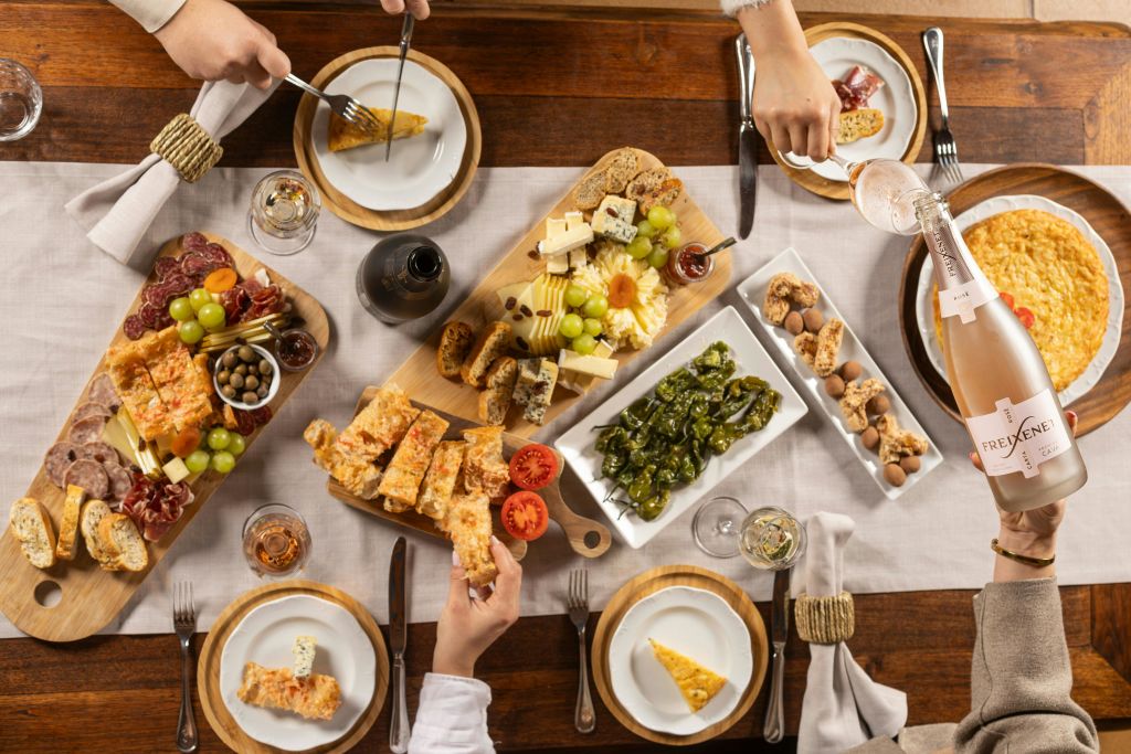 다양한 치즈, 포도, 빵 및 기타 애피타이저가 놓인 식탁의 오버헤드 뷰입니다. 4명이 음식을 주문할 수 있습니다.