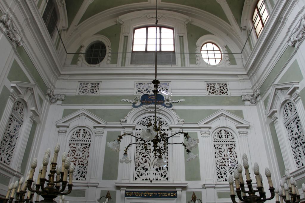 높은 천장의 방에는 아치형 창문, 하얀 벽의 정교한 조각, 중앙 샹들리에가 있는 화려한 인테리어가 돋보입니다.