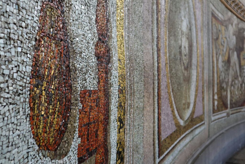 복잡한 패턴과 흙빛 톤과 금색 악센트가 어우러진 디테일한 모자이크 벽의 클로즈업.