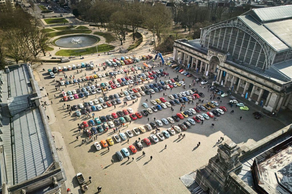 역사적인 건물 앞에 다채로운 색상의 자동차가 줄지어 서 있고 사람들이 돌아다니는 자동차 쇼의 공중 전망.