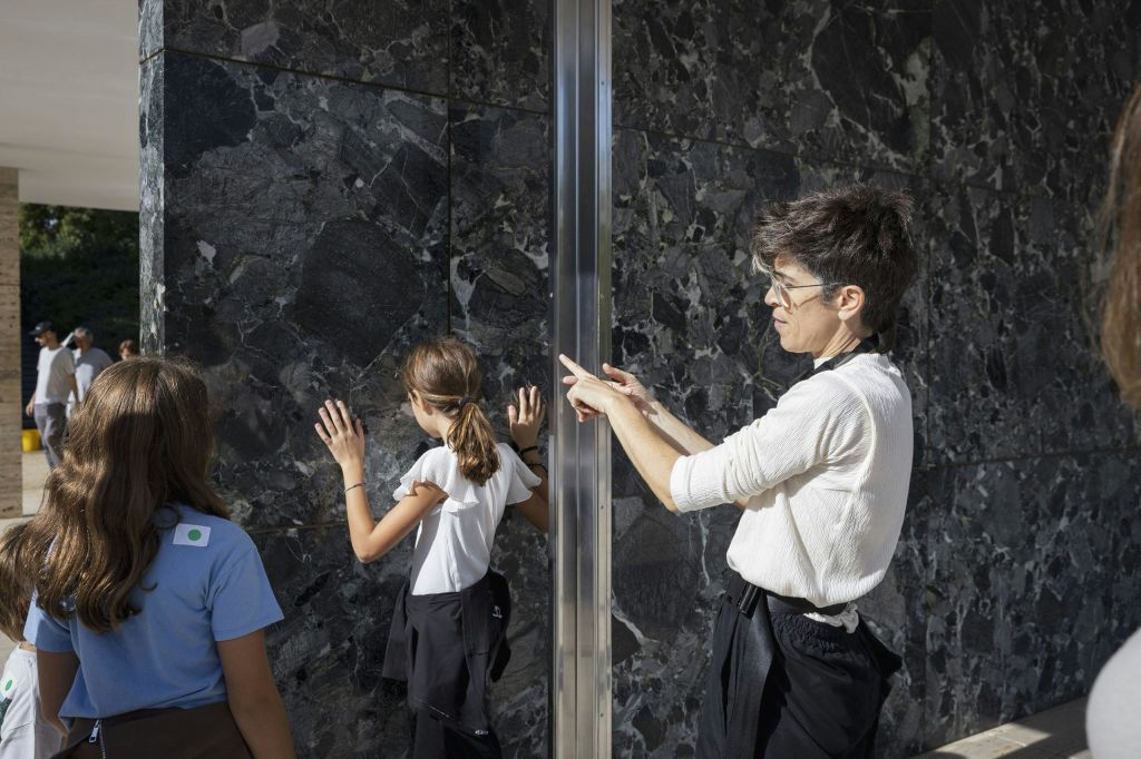 흰색 셔츠를 입은 사람이 반사 표면 근처에 손을 대고 제스처를 취하는 반면, 다른 사람은 표면을 바라봅니다.