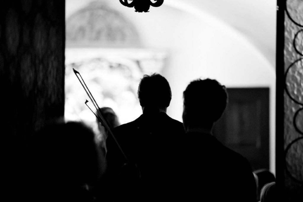 화려한 배경의 어두운 조명 방에서 바이올린을 들고 있는 사람들의 실루엣.