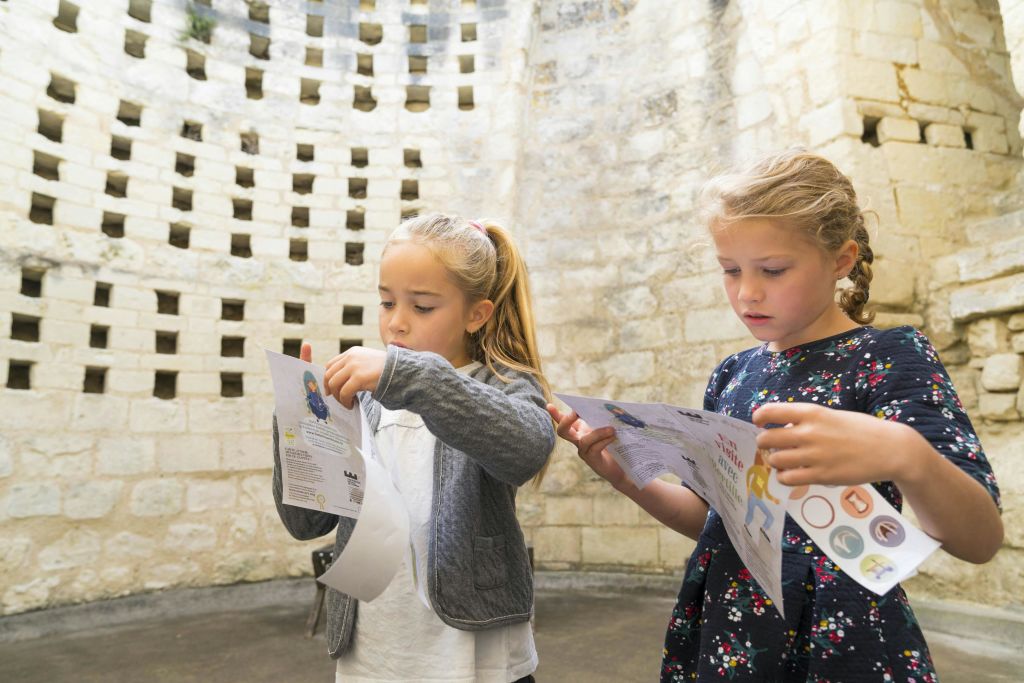 두 어린 소녀가 오래된 돌담 앞에 서서 그림이 있는 종이를 살펴보고 있습니다.