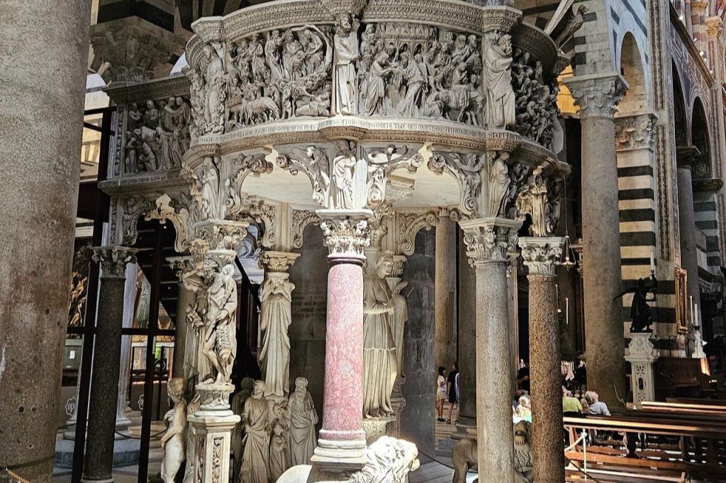 사람들이 배경으로 한 유서 깊은 건물에서 기둥으로 받쳐주는 섬세한 종교적 조각이 돋보이는 화려한 석조 강단.
