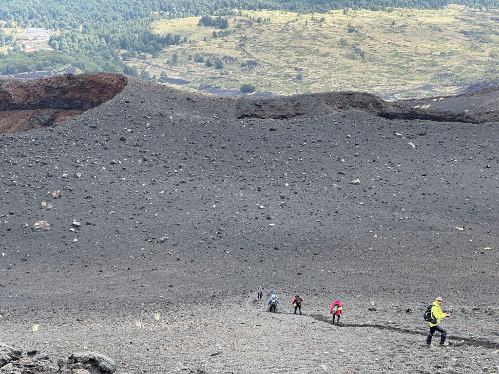 먼 풍경을 배경으로 흩어진 돌로 둘러싸인 바위 화산 지대를 하이킹하는 사람들.