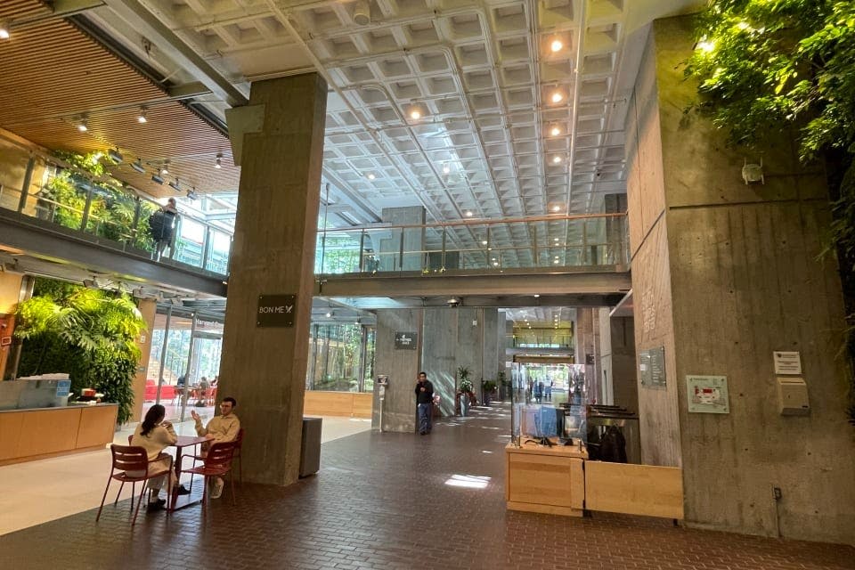 천장이 높은 넓은 아트리움에는 현대적인 인테리어, 커다란 창문, 테이블에 앉아 산책하는 사람들이 있습니다.