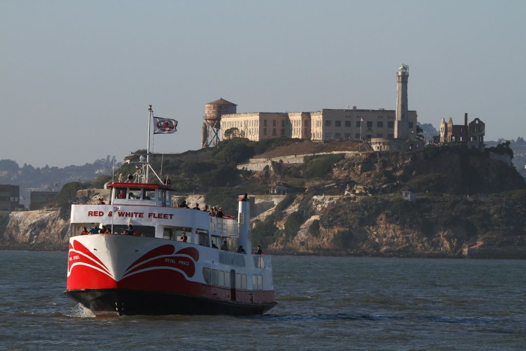 이전 감옥과 급수탑이 보이는 Alcatraz Island 앞에 "빨간색 및 흰색 함대" 라고 표시된 페리가 항해합니다.