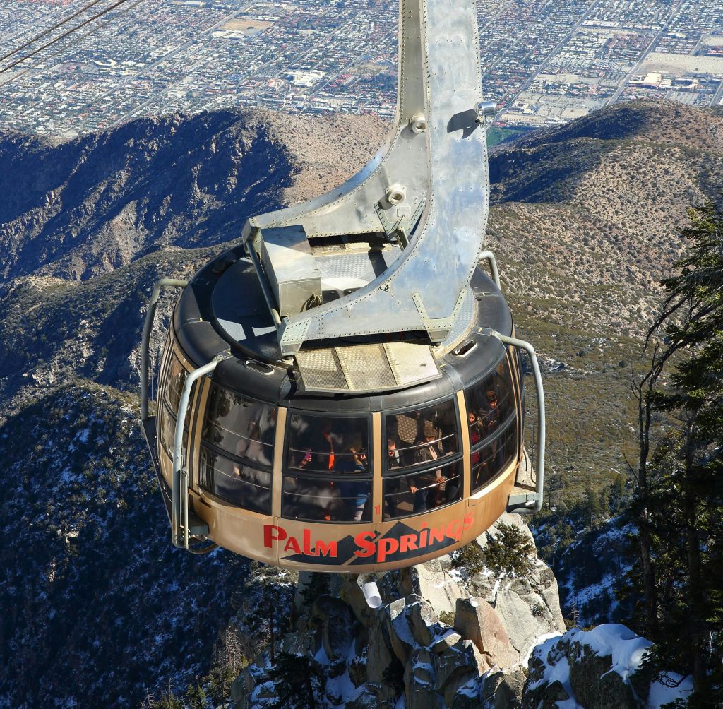도시 풍경을 배경으로 산악 지형을 오르는 '팜스프링스' 라는 이름의 공중 전차.