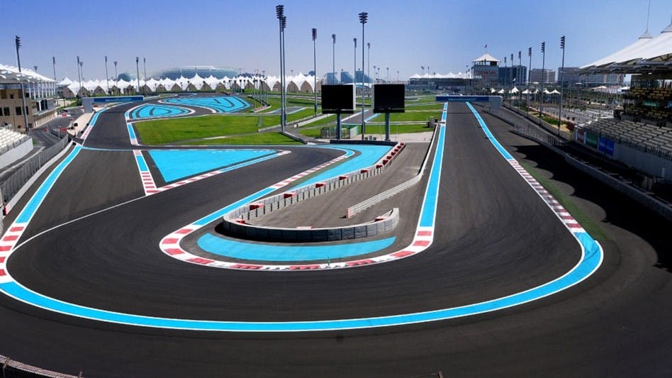 잔디, 그랜드스탠드, 두 개의 대형 스크린으로 둘러싸인 파란색과 흰색 표시가 있는 빈 레이스 트랙입니다.