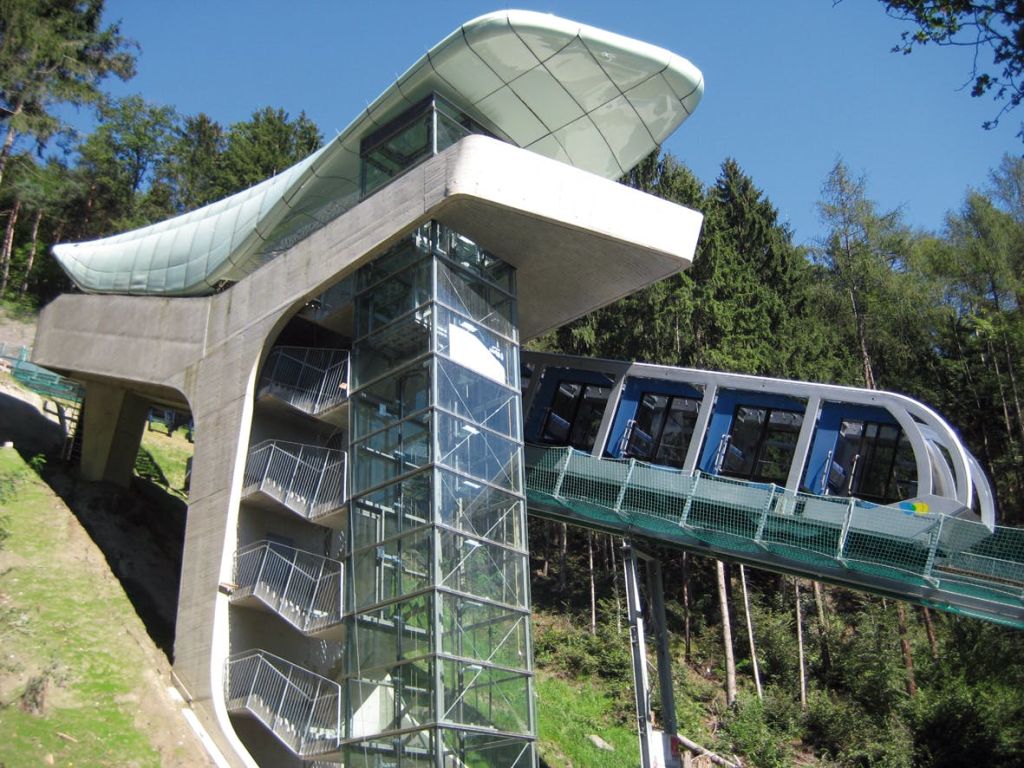 유리 계단 구조와 숲이 우거진 언덕을 통과하는 경사진 기차가 있는 현대적인 푸니쿨라 철도입니다.