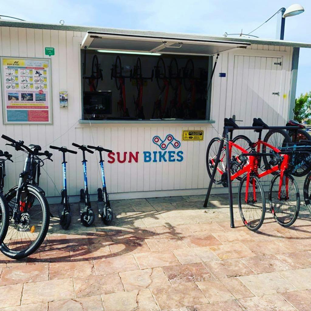"Sun Bikes" 라고 표시된 자전거 대여 키오스크에는 자전거와 전동 스쿠터가 외부에 전시되어 있습니다.