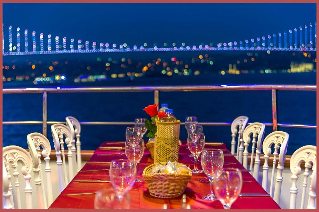 밤하늘 아래 와인잔과 바구니가 놓인 저녁 식사용 테이블에 불이 켜진 다리가 배경으로 놓여 있습니다.