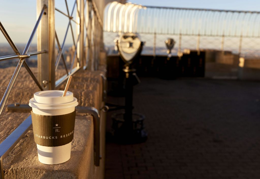 햇살이 내리쬐는 야외 환경에서 전망 파인더와 난간이 있는 선반에 놓인 스타벅스 리저브 커피잔.
