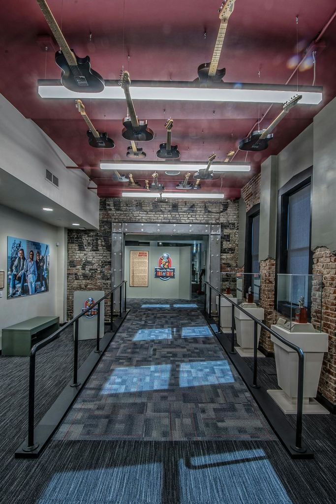 매달린 기타, 전시 케이스, 노출된 벽돌 벽 및 좌석 방문객이 보이는 벽화가 있는 박물관 복도입니다.