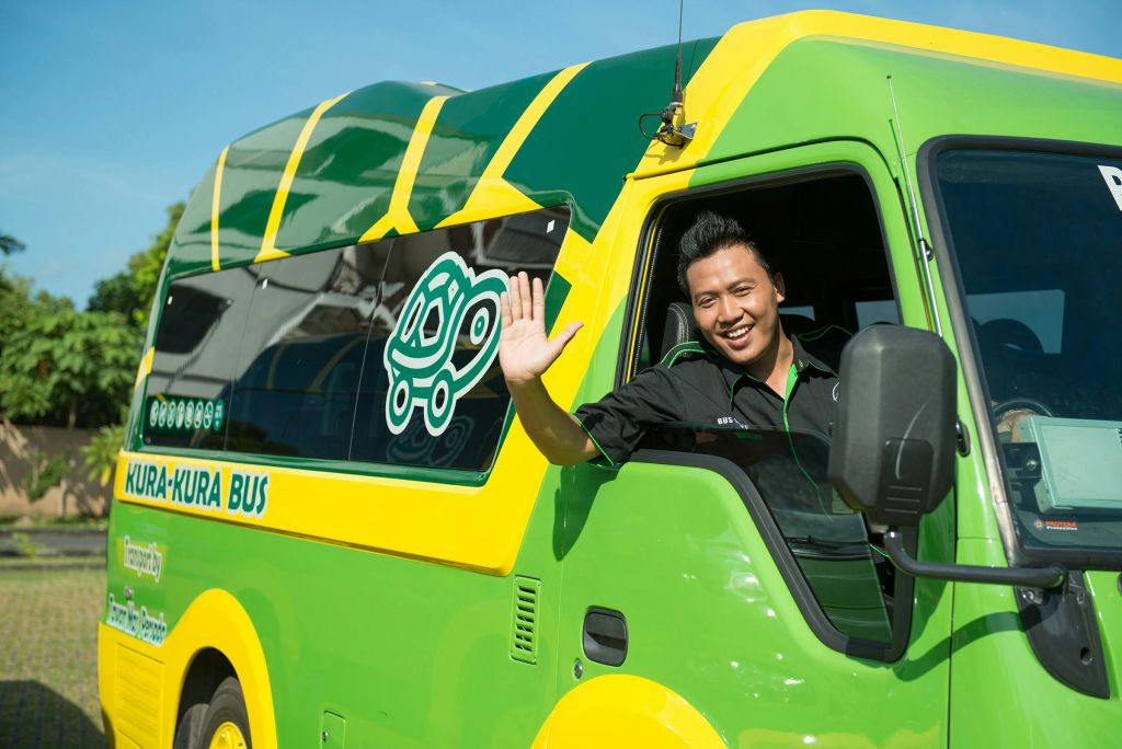 옆면에 만화 거북이 그래픽이 그려진 초록색과 노란색 차량의 운전석에서 미소를 짓고 손을 흔드는 남성.