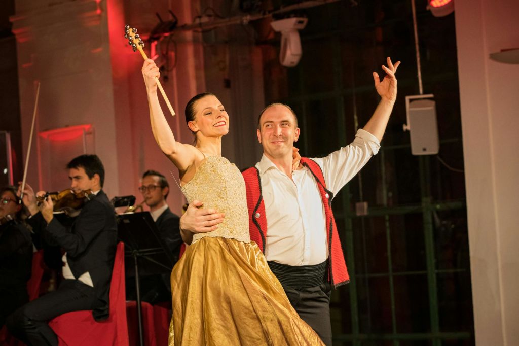 따뜻한 실내 환경에서 바이올린을 연주하는 음악가들에게 둘러싸인 우아한 복장을 한 남녀가 춤을 추고 있습니다.