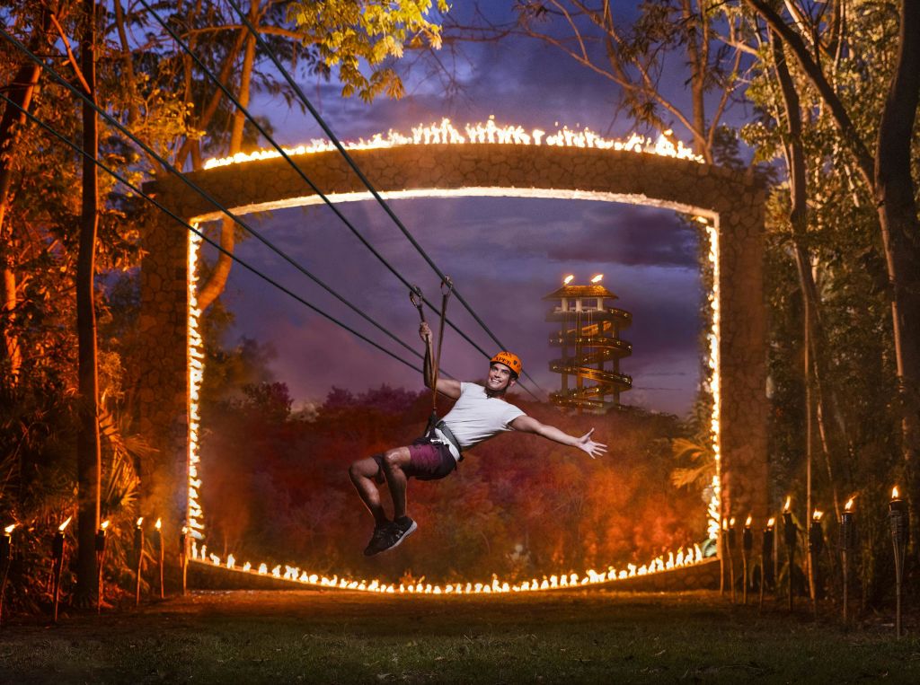 해질 무렵 나선형 타워와 나무를 배경으로 불타는 반지 사이로 헬멧을 착용한 사람이 집업하고 있습니다.