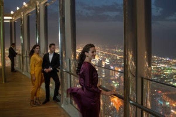 우아한 차림의 세 사람이 야간에 높은 전망대에 올라 밝게 빛나는 도시 풍경을 내려다보고 있습니다.