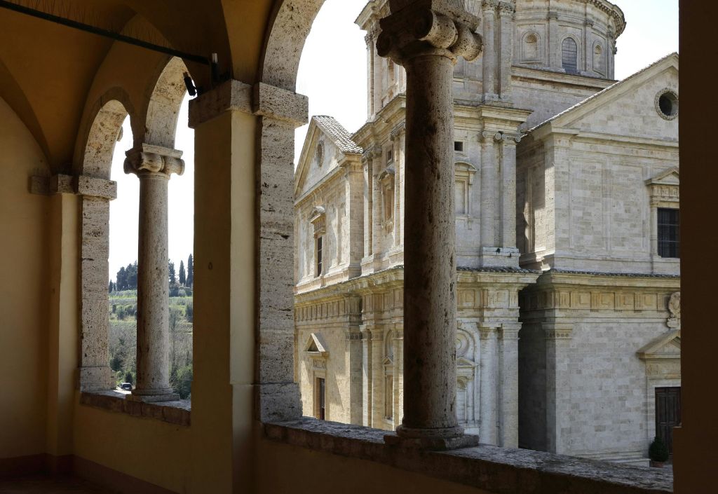 전경에 기둥이 있고 멀리 풍경이 보이는 일련의 아치를 통해 유서 깊은 석조 건물의 전망.