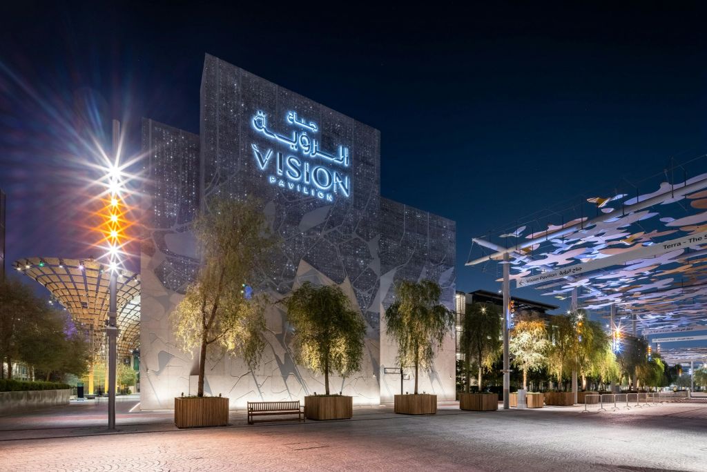 광장의 나무와 벤치로 둘러싸인 '비전 파빌리온 (Vision Pavilion)' 이라는 이름의 현대적인 야간 조명 건물입니다.