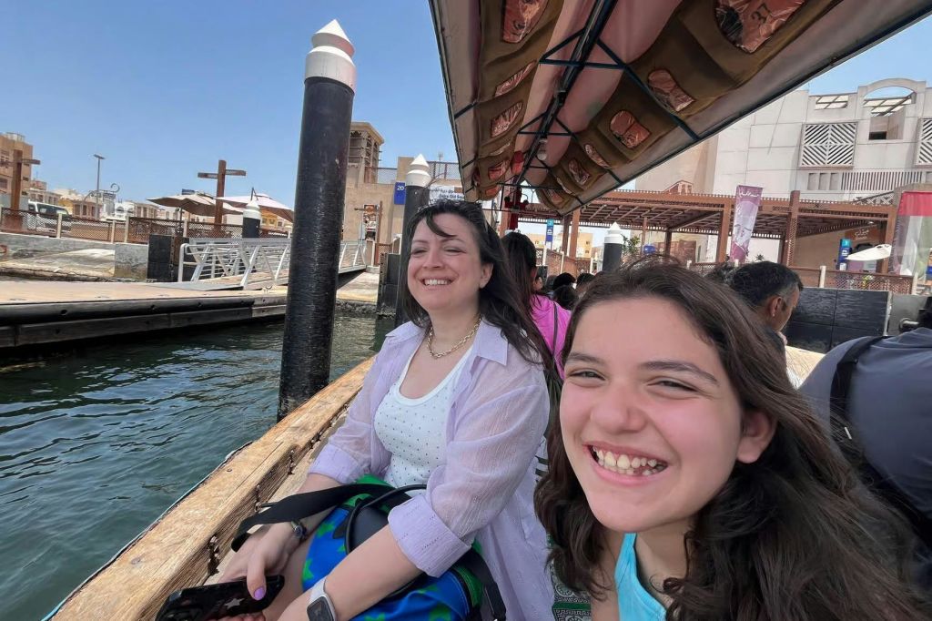 선착장 근처에서 보트를 타고 미소를 짓고 있는 두 사람으로, 머리 위에는 지붕이 덮여 있고 그 뒤로 물이 흐르고 있습니다.